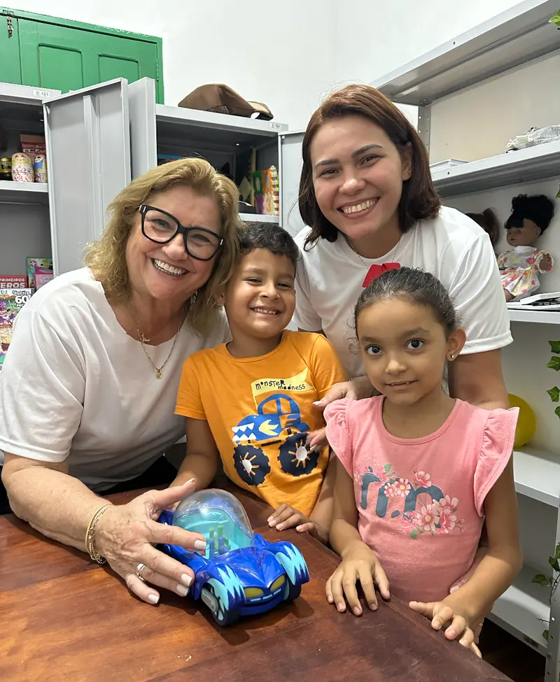 Psicólogas da Zoé sorrindo ao lado de duas crianças na sala de atendimento